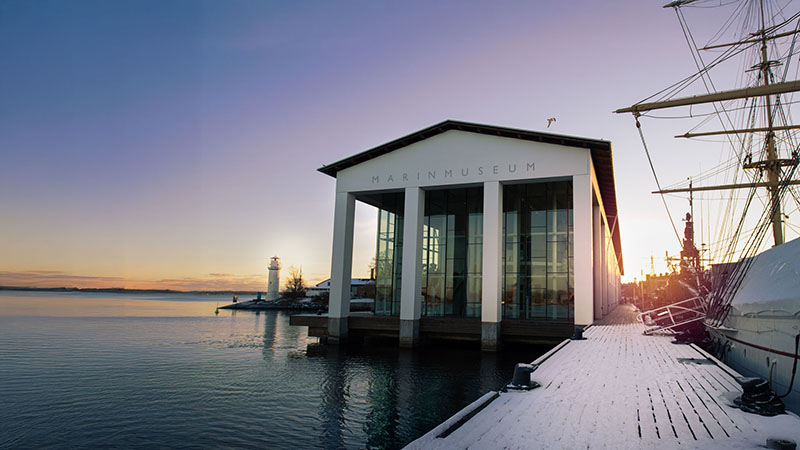 Vy över Marinmuseums byggnad, ett högt vitt hus, vid vatten. 